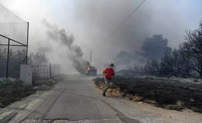 A man runs while flames burn a mini excavator during a fire in northern Athens, Monday, Aug. 12, 2024, as hundreds of firefighters tackle a major wildfire raging out of control on fringes of Greek capital. (AP Photo/Michael Varaklas)