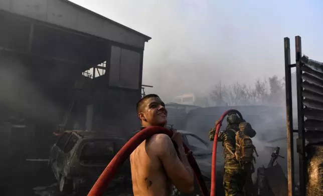 Two men try to extinguish the flames at a burning business during a fire in northern Athens, Monday, Aug. 12, 2024, as hundreds of firefighters tackle a major wildfire raging out of control on fringes of Greek capital. (AP Photo/Michael Varaklas)