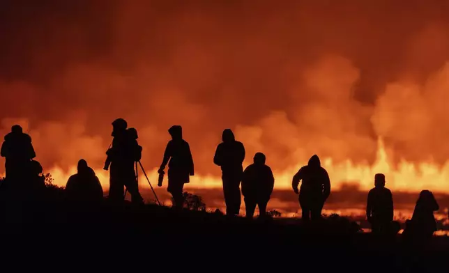 Tourists and visitors try to get a view of a volcanic eruption from a distance at the intersection between Reykjanesbraut, Iceland, and the road to Grindavik, Thursday, Aug. 22, 2024. (AP Photo/Marco di Marco)