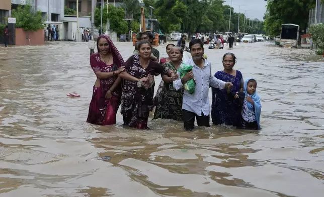 A family wades through a flooded road after heavy rain in Ahmedabad, India, Monday, Aug. 26, 2024. (AP Photo/Ajit Solanki)