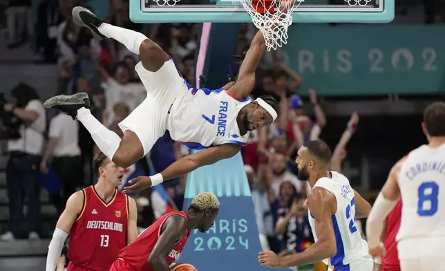 Guerschon Yabusele, of France, hangs on the rim after a dunk against Germany in a men's basketball game at the 2024 Summer Olympics, Friday, Aug. 2, 2024, in Villeneuve-d'Ascq, France. (AP Photo/Mark J. Terrill)