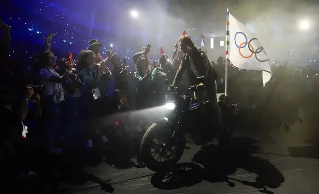 Tom Cruise rides a motorbike with the Olympic flag attached during the 2024 Summer Olympics closing ceremony at the Stade de France, Sunday, Aug. 11, 2024, in Saint-Denis, France. (AP Photo/Ashley Landis)