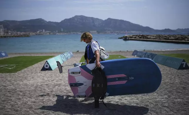 Elia Colombo of Switzerland carries his windsurf board after the men's windsurfing medal race was postponed until Saturday due to lack of wind during the 2024 Summer Olympics, Friday, Aug. 2, 2024, in Marseille, France. (AP Photo/Daniel Cole)