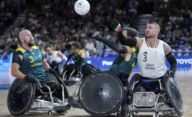 Andrew Edmondson of Australia, center, and Stuart Robinson of Great Britain, right, challenge for the ball as Ryley Batt of Australia looks on during the 2024 Paralympics Wheelchair Rugby match Australia against Great Britain at the Champs Mars Arena Thursday, Aug. 29, 2024, in Paris, France. (AP Photo/Michel Euler)