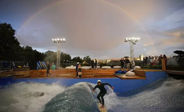 A rainbow arcs in the sky as a man surfs in a wave pool at Muzeon park in Moscow, Russia, on Sunday, Aug. 11, 2024. (AP Photo/Pavel Bednyakov)