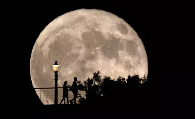 People walk in front of a rising supermoon at Griffith Observatory in Los Angeles, Monday, Aug. 19, 2024. (AP Photo/Richard Vogel)