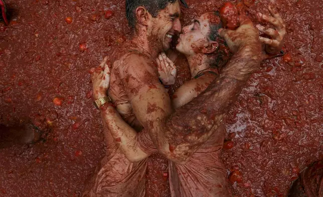 Revelers lie in a pool of squashed tomatoes during the annual "Tomatina" tomato fight fiesta, in the village of Bunol near Valencia, Spain, Wednesday, Aug. 28, 2024. (AP Photo/Alberto Saiz)