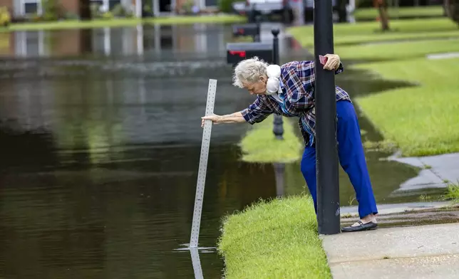 A resident measures the depth of the flooded street with storm water from Tropical Storm Debby, Wednesday, Aug. 7, 2024 Pooler, Ga. (AP Photo/Stephen B. Morton)