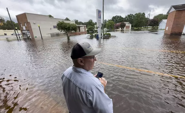 Randy Sikes speaks to his relatives on a mobile phone as he stands in residual rain water flooding the downtown area caused by Tropical Storm Debby, Thursday, Aug. 8, 2024, in Bladenboro, NC. (AP Photo/John Minchillo)