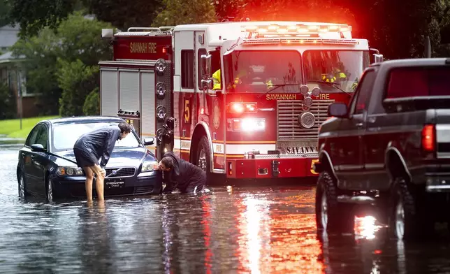 People attach a towline to a stranded vehicle on a flooded street after heavy rain from Tropical Storm Debby, Monday, Aug. 5, 2024, in Savannah, Ga. (AP Photo/Stephen B. Morton)