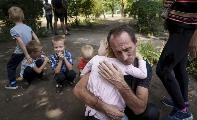 A father hugs his daughter, his other children nearby, as they wait for evacuation in Pokrovsk, Donetsk region, Ukraine, Friday, Aug. 23, 2024. (AP Photo/Evgeniy Maloletka)