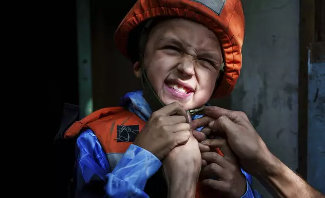 A Fenix team rescue worker places a helmet on Bohdan Scherbyna, 9, as he is evacuated with his mother Maryna Scherbyna and 14 year old sister Angelina Scherbyna, as local people as moved from Selidove to safe areas, in Pokrovsk, Donetsk region, Ukraine, on Tuesday, Aug. 20, 2024. (AP Photo/Evgeniy Maloletka)