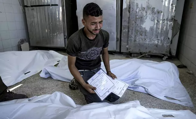 A Palestinian man mourns his 4-day-old twin relatives, killed in the Israeli bombardment of the Gaza Strip, as he holds their birth certificates, at a hospital morgue in Deir al-Balah, Tuesday, Aug. 13, 2024. (AP Photo/Abdel Kareem Hana)