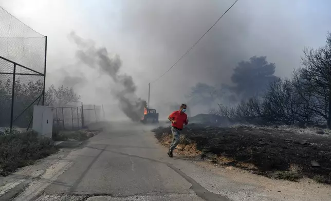 A man runs while flames burn a mini excavator during a fire in northern Athens, Monday, Aug. 12, 2024, as hundreds of firefighters tackle a major wildfire raging out of control on fringes of Greek capital. (AP Photo/Michael Varaklas)