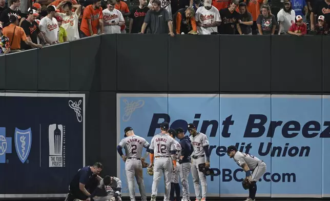 Houston Astros left fielder Mauricio Dubón sits on the ground and is seen by the trainer after running into the wall to make a catch during the seventh inning of a baseball game against the Baltimore Orioles, Sunday, Aug. 25, 2024, in Baltimore. (AP Photo/Terrance Williams)