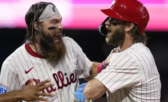 Philadelphia Phillies' Bryce Harper, right, and Brandon Marsh celebrate after Harper hit a game-winning RBI-single against Houston Astros pitcher Josh Hader during the 10th inning of a baseball game, Monday, Aug. 26, 2024, in Philadelphia. (AP Photo/Matt Slocum)