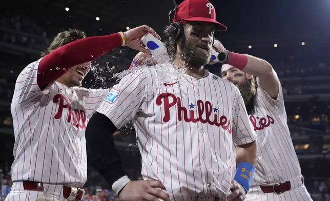 Philadelphia Phillies' Bryce Harper, center, is doused by Bryson Stott, left, and Brandon Marsh after hitting the game-winning RBI-single against Houston Astros pitcher Josh Hader during the 10th inning of a baseball game, Monday, Aug. 26, 2024, in Philadelphia. (AP Photo/Matt Slocum)