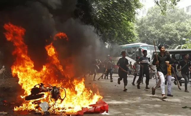 FILE - Men run past a burning vehicle inside the Bangabandhu Sheikh Mujib Medical University Hospital, set on fire by protesters, during a rally against Prime Minister Sheikh Hasina and her government demanding justice for the victims killed in the recent countrywide deadly clashes, in Dhaka, Bangladesh, on Aug. 4, 2024. (AP Photo/Rajib Dhar, File)