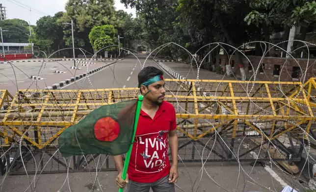 A protester carries Bangladesh flag as he and others block the road in front of the former residence of Sheikh Mujibur Rahman, father of the ousted Prime Minister Sheikh Hasina, on his death anniversary in Dhaka, Bangladesh, Thursday, Aug. 15, 2024. (AP Photo/Rajib Dhar)