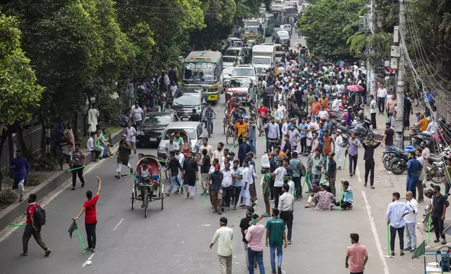 Protesters carry sticks and Bangladesh flags as they block the road in front of the former residence of Sheikh Mujibur Rahman, father of the ousted Prime Minister Sheikh Hasina, on his death anniversary in Dhaka, Bangladesh, Thursday, Aug. 15, 2024. (AP Photo/Rajib Dhar)