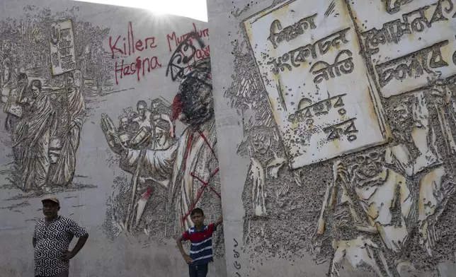 People stand near vandalised murals of Sheikh Mujibur Rahman, father of Sheikh Hasina who resigned as Prime Minister on Monday, in Dhaka, Bangladesh, Tuesday, Aug. 6, 2024. (AP Photo/Fatima Tuj Johora)