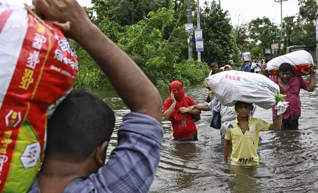 People walk to a relief shelter with belongings through a flooded street following heavy rains in Mohipal, Feni, a coastal district in southeast Bangladesh, Friday, Aug. 23, 2024. (AP Photo/Fatima Tuj Johora)