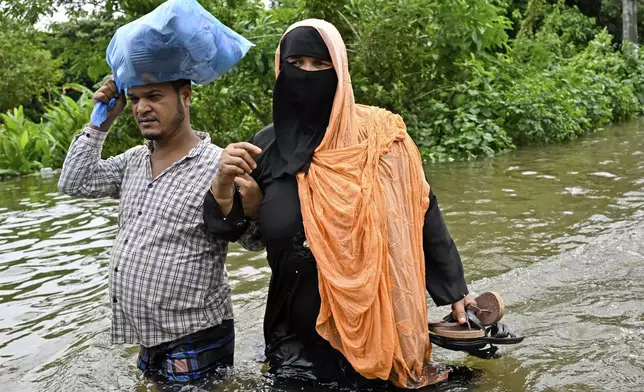 People walk to a relief shelter with their belongings through a flooded street in Mohipal, Feni, a coastal district in southeast Bangladesh, Friday, Aug. 23, 2024. (AP Photo/Fatima Tuj Johora)