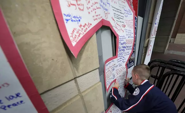 Gavin Rose signs a number thirteen at a memorial set up by fans for Blue Jackets hockey player Johnny Gaudreau in Columbus, Ohio, Aug. 30, 2024. Gaudreau, along with his brother Matthew, was fatally struck by a motorist while riding his bicycle on Thursday. (AP Photo/Joe Maiorana)