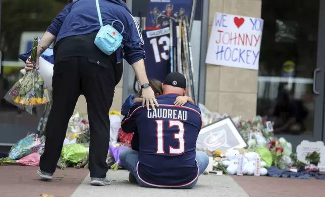 Hylas Stemen, sitting, of Columbus, mourns at a memorial set up by fans for Blue Jackets hockey player Johnny Gaudreau in Columbus, Ohio, Aug. 30, 2024. Gaudreau, along with his brother Matthew, was fatally struck by a motorist while riding his bicycle on Thursday. (AP Photo/Joe Maiorana)