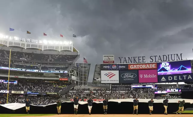 Members of the ground crew cover the field during a rain delay in the eighth inning of a baseball game between the New York Yankees and the Toronto Blue Jays at Yankee Stadium, Sunday, Aug. 4, 2024, in New York. (AP Photo/Seth Wenig)