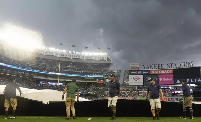 Members of the ground crew cover the field during a rain delay in the eighth inning of a baseball game between the New York Yankees and the Toronto Blue Jays at Yankee Stadium Sunday, Aug. 4, 2024, in New York. (AP Photo/Seth Wenig)