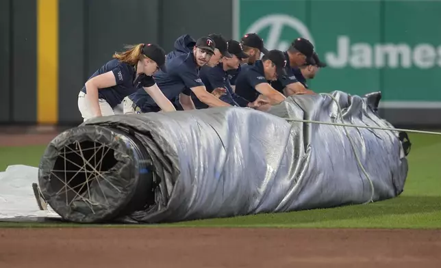 Grounds crew members roll the tarp into the field during a weather delay of a baseball game between the Minnesota Twins and the Atlanta Braves, Monday, Aug. 26, 2024, in Minneapolis. (AP Photo/Abbie Parr)