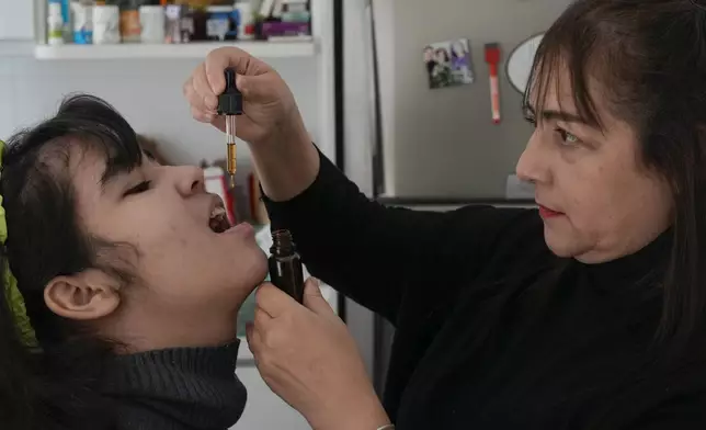 Maria Aparecida Carvalho gives a dose of liquid cannabidiol or CBD, to her daughter Clárian, diagnosed with Dravet Syndrome, at their home in Sao Paulo, Wednesday, July 10, 2024. Clárian was diagnosed at age 10 with Dravet Syndrome, a severe form of epilepsy that can cause cardiorespiratory arrests and lead to sudden death. (AP Photo/Andre Penner)