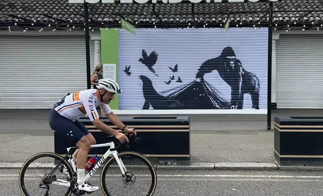 A cyclist rides by the reproduction of a Banksy mural outside the London Zoo, Sunday, Aug. 18, 2024. The London Zoo has removed Banksy's gorilla mural from its entrance gate. The painting was the final animal-themed work by the street artist that appeared over nine consecutive days in London. (AP Photo/Brian Melley)