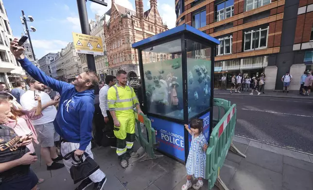 A man takes a selfie by a new design of swimming fish by Banksy, which appeared on a police box in the City of London is cordoned off, in London, Monday Aug. 12, 2024. (Emily Pennink/PA via AP)