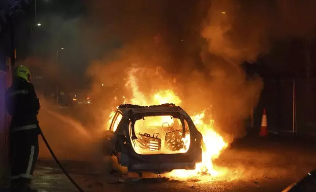 Firefighters tend to a burning police car as police officers are deployed on the streets of Hartlepool, England, following a violent protest in the wake of the killing of three girls who were fatally stabbed in northwest England, Wednesday, July 31, 2024. (Owen Humphreys/PA via AP)