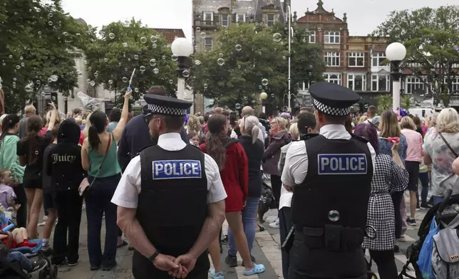 Police officers watch members of the public outside the Town Hall during a vigil to remember the victims of the stabbing attack last Monday in Southport, England, Monday, Aug. 5, 2024. Violence and unrest erupted in cities and towns across Britain, ostensibly in protest of last week's stabbing. (AP Photo/Darren Staples)