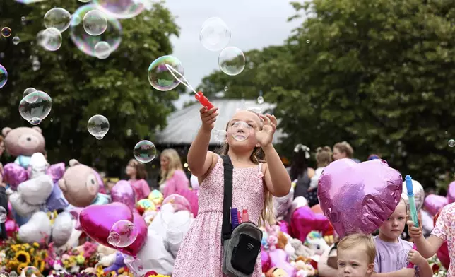 Children form bubbles outside the Town Hall during a vigil to remember the victims of the stabbing attack last Monday in Southport, England, Monday, Aug. 5, 2024. Violence and unrest erupted in cities and towns across Britain, ostensibly in protest of last week's stabbing. (AP Photo/Darren Staples)