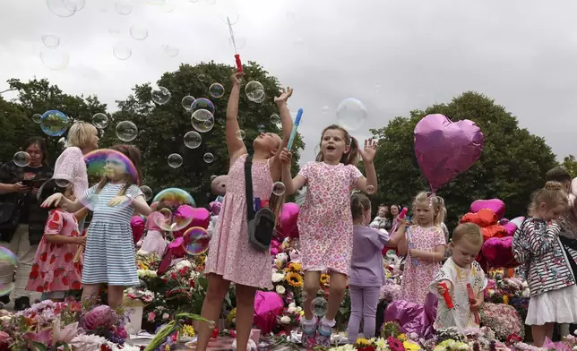 Children form bubbles outside the Town Hall during a vigil to remember the victims of the stabbing attack last Monday in Southport, England, Monday, Aug. 5, 2024. Violence and unrest erupted in cities and towns across Britain, ostensibly in protest of last week's stabbing. (AP Photo/Darren Staples)