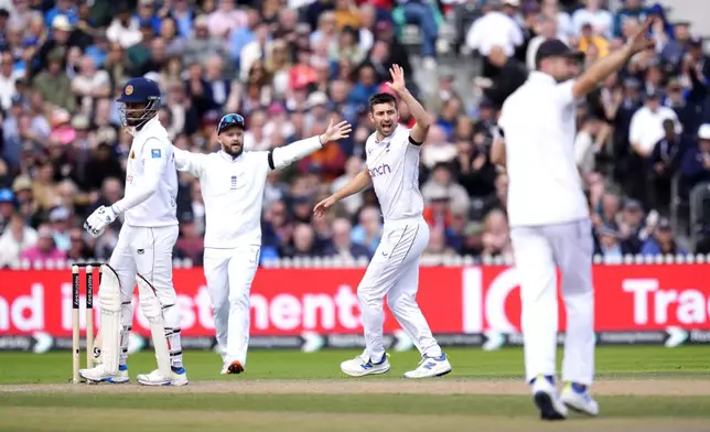 Sri Lanka's Dimuth Karunaratne, left, leaves the pitch after being caught by England's Harry Brook bowled by Mark Wood, center, on day three of the First Test match between England and Sri Lanka at Emirates Old Trafford, Manchester, England, Friday Aug. 23, 2024. (Nick Potts/PA via AP)