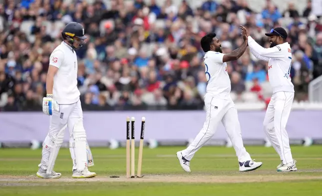 Sri Lanka's Asitha Fernando, center, celebrates with teammate Prabath Jayasuriya after bowling out England's Ollie Pope, left, on day two of the First Test match between England and Sri Lanka at Emirates Old Trafford, Manchester, England, Thursday Aug. 22, 2024. (Nick Potts/PA via AP)