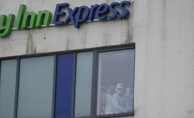 People watch from a window inside the Holiday Inn Express as an anti-immigration demonstration takes place outside the hotel, in Rotherham, England, Sunday Aug. 4, 2024. (Danny Lawson/PA via AP)