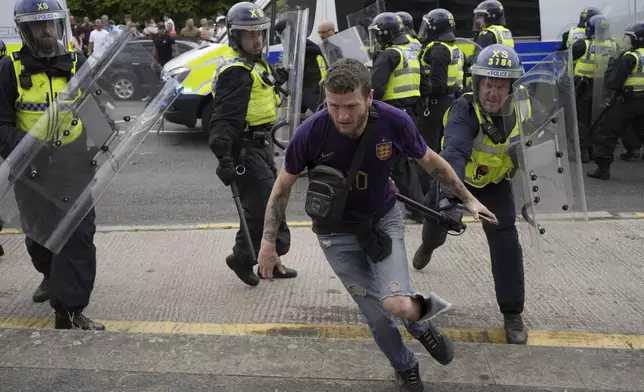 Police officers chase a protester as trouble flares during an anti-immigration protest outside the Holiday Inn Express in Rotherham, England, Sunday Aug. 4, 2024. (Danny Lawson/PA via AP)