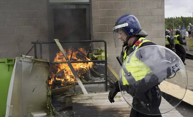 A police officer walks past a fire as trouble flares during an anti-immigration protest outside the Holiday Inn Express in Rotherham, England, Sunday Aug. 4, 2024. (Danny Lawson/PA via AP)