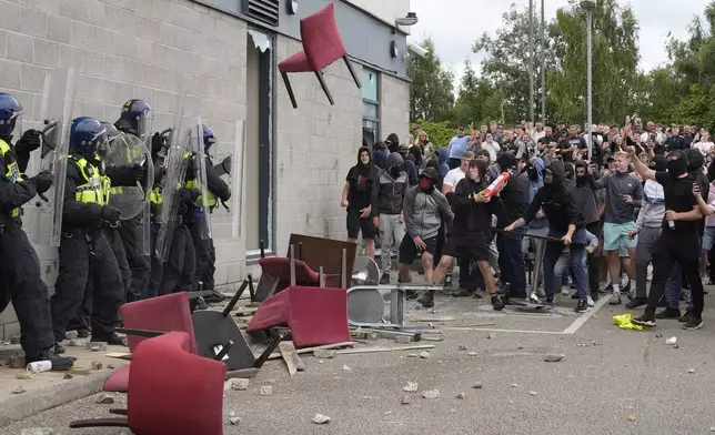 A chair is thrown at police officers as trouble flares during an anti-immigration protest outside the Holiday Inn Express in Rotherham, England, Sunday Aug. 4, 2024. (Danny Lawson/PA via AP)