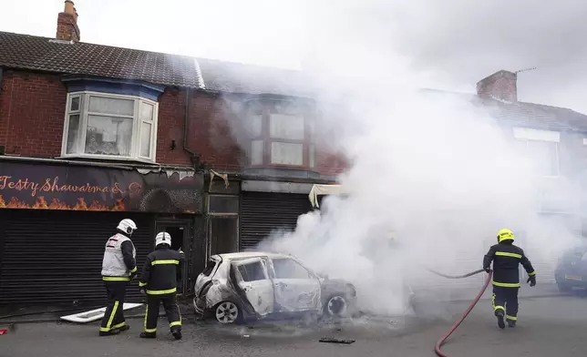 Firefighters extinguish a burning car on Parliament Road, during an anti-immigration protest in Middlesbrough, England, Sunday Aug. 4, 2024. (Owen Humphreys/PA via AP)