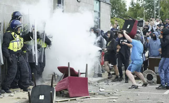 A protester uses a fire extinguisher on police officers as trouble flares during an anti-immigration protest outside the Holiday Inn Express in Rotherham, England, Sunday Aug. 4, 2024. (Danny Lawson/PA via AP)