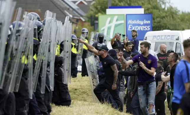 Demonstrators face police officers as trouble flares during an anti-immigration protest outside the Holiday Inn Express in Rotherham, England, Sunday Aug. 4, 2024. (Danny Lawson/PA via AP)