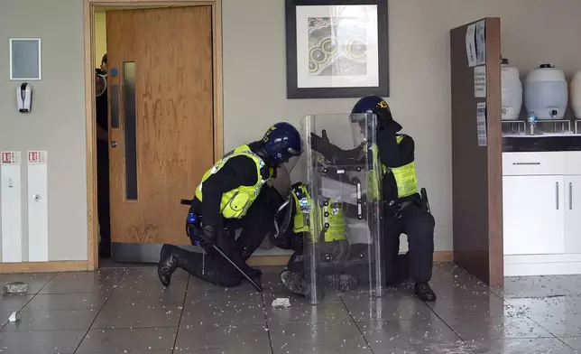 Police officers tend to a wounded colleague inside the hotel as seen through a smashed window as trouble flares during an anti-immigration protest outside the Holiday Inn Express in Rotherham, England, Sunday Aug. 4, 2024. (Danny Lawson/PA via AP)