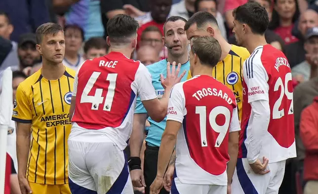 Arsenal's Declan Rice, second left, discusses with referee Chris Kavanagh, center, during the English Premier League soccer match between Arsenal and Brighton, at Emirates Stadium in London, Saturday, Aug. 31, 2024. (AP Photo/Alastair Grant)